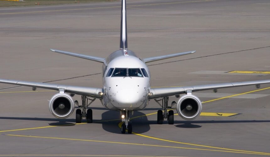 Parked commercial aircraft at airport terminal with ground service vehicles nearby.